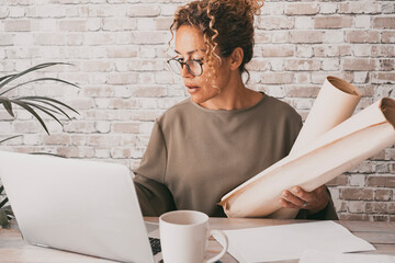 Wall Mural - Mature student using computer and papers at home at the desk. Office woman working on laptop with connection. Confident portrait of female people and modern job activity. Architect lady in the studio