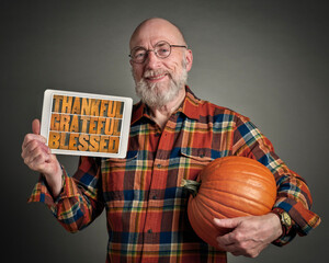 Wall Mural - thankful, grateful and blessed - senior man with pumpkin is holding a digital tablet with sign in letterpress wood type, Thanksgiving concept