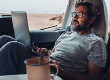 Concept Of Travel Lifestyle Modern People And Smart Working Digital Nomad Job Activity. Handsome Man Use Laptop Computer Sitting And Relaxing Inside A Camper Van Vehicle Parked At The Beach. Freedom