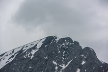 Monochrome Scenery With High Mountain Peak With Snow Cornice In Gray Cloudy Sky At Overcast. Dark Atmospheric Mountain Landscape With Large Pinnacle In Lead Gray Sky At Rainy Weather In Grayscale.