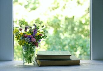 Wall Mural - Beautiful meadow flowers in glass and old books on wooden table, abstract green natural background. Summer season. floral composition in rustic style. reading, relax concept