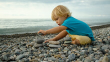 A Child Plays With Stones On The Beach. 