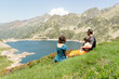© Esther Pueyo - Couple and their toddler sitting on a green slope enjoying the aerial view of a mountain lake called lac d'artouste located in french pyrenees. Active family vacations.