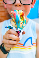 a boy in a tank top holds a very messy and melting multicolored ice cream cone on a very hot day