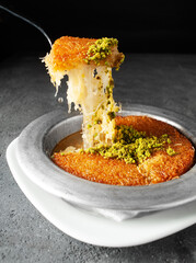 Turkish dessert kunefe, kunafa, kadayif with pistachio powder and cheese, served hot, very sweet. Turkish traditional dessert on grey background