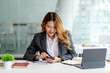 © amnaj - Beautiful young Asian businesswoman with a smile sitting using smartphone at the office.