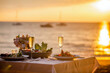 © TravelMedia - Romantic sunset dinner on the beach. Table honeymoon set for two with luxurious food, glasses of champagne drinks in a restaurant with sea view. Summer love, romance date on vacation concept.