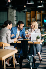 Group of colleagues talk while working on laptop during business meeting in cafe.