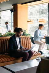 Young smiling businessman working on laptop in cafe.