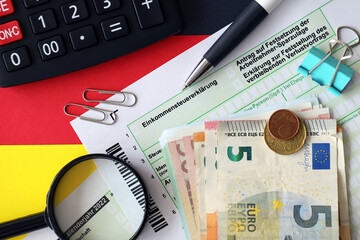 German income tax return form with pen and european euro money bills lies on flag close up. Taxpayers in Germany using euro currency to pay taxes