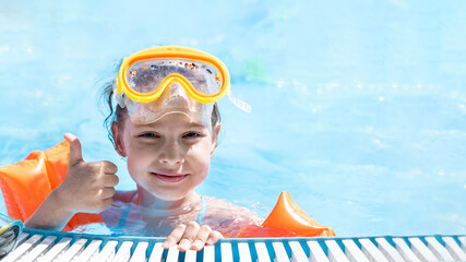 Close-up portrait of a cute little Caucasian girl swimming in the pool in a swimming mask and armbands, beach resort, summer vacation concept. Space for text.