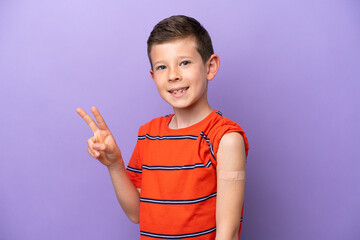 Wall Mural - Little boy wearing a band aid isolated on purple background smiling and showing victory sign