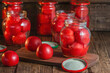 canning of red ripe tomatoes in their own juice, on a wooden background there are glass jars in which peeled tomatoes are stacked