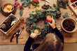 © Mediaphotos - High angle view of busy woman standing at desk and using decorative ribbon while making Christmas wreath