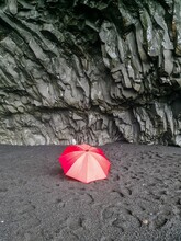 A Lone Red Umbrella On The Endless Black Beaches Of Iceland In Front Of Black Basalt Rock Formations.