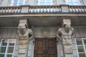 Four elegant stone Atlantes supports central balcony of historic building of Tyszkiewicz-Potocki Palace in Warsaw. Sculptures were carved in 1787 by Andre Le Brun