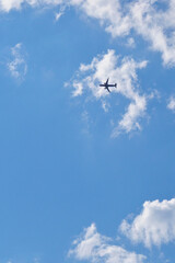 Wall Mural - The passenger airplane is flying far away in the blue sky and white clouds. Aircraft in the air. Light vertical background or illustration about international passenger air transportation