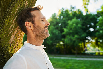 Mid adult man leaning against a tree with eyes closed in a park