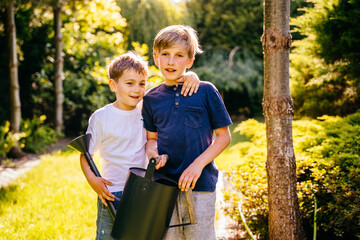 Two children watering organic garden plats at backyard with watering can in garden.