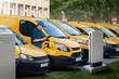 © scharfsinn86 - A man with a digital tablet stands next to yellow electric delivery vans at electric vehicle charging stations