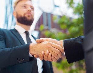 Wall Mural - Handshake close-up. Businessman and his colleague are shaking hands in front of modern office building. Financial investors outdoor. Banking and business concept.