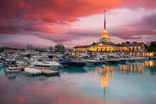 Sea Port Of Sochi, Russia. Yacht And Boats In Marine Station. Beautiful Cityscape At Sunset, Pink Clouds Are Reflected In Calm Water.