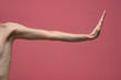 Young woman's stretched skinny arm with stop gesture. Isolated on pink background