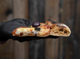 Food. closeup view of the chef's hand wearing gloves, holding and presenting a slice of pizza with mozzarella cheese, bell pepper, ham, black olives and oregano.