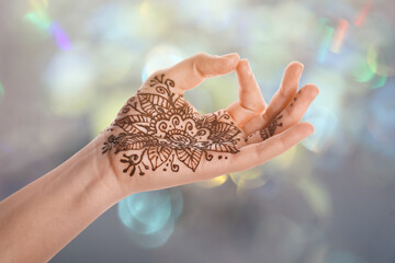 Woman with henna tattoo on palm against blurred lights, bokeh effect