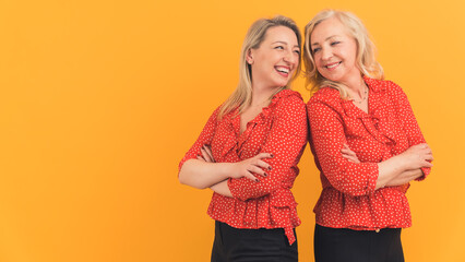 Two attractive cheerful women in their 40s in similar outfits, standing back to back with their arms crossed, smiling and laughing. High quality photo