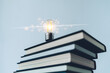 © Koto Amatsukami - Glowing lightbulb or bright lamp with book or textbook. Skill improvement for student or businessperson. Studying and training course online at home. Business success idea, education learning concept