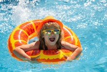 Kid Boy In Swimming Pool On Inflatable Ring. Children Swim With Orange Float. Water Toy, Healthy Outdoor Sport Activity For Children. Kids Beach Fun. Child Splashing In Summer Water Pool.