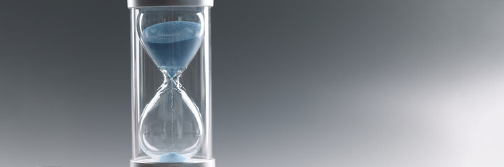 Closeup of hourglass with blue sand on gray background