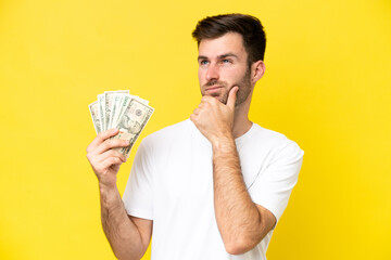 Wall Mural - Young caucasian man taking a lot of money isolated on yellow background having doubts