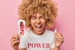 Emotional curly haired woman screams loudly holds sanitary napkin and tampon tries to make right feminine hygiene choice dressed in casual t shirt isolated over pink background. Sanitary products
