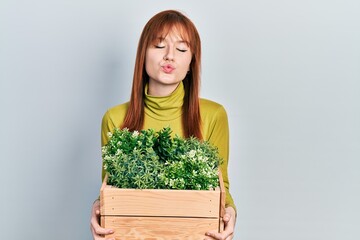 Sticker - Redhead young woman holding wooden plant pot looking at the camera blowing a kiss being lovely and sexy. love expression.