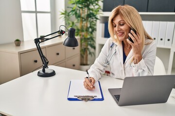 Wall Mural - Middle age blonde woman wearing doctor uniform talking on the smartphone at clinic