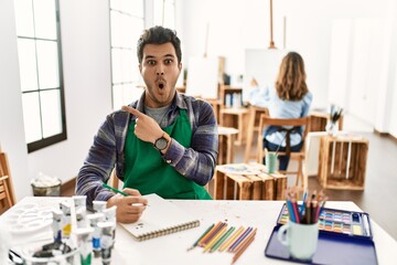 Poster - Young artist man at art studio surprised pointing with finger to the side, open mouth amazed expression.