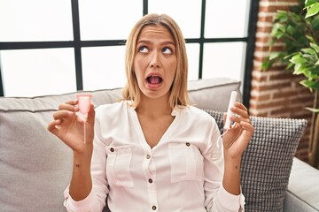 Canvas Print - Young blonde woman holding menstrual cup and tampon angry and mad screaming frustrated and furious, shouting with anger looking up.