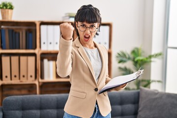 Canvas Print - Young hispanic woman working at consultation office annoyed and frustrated shouting with anger, yelling crazy with anger and hand raised