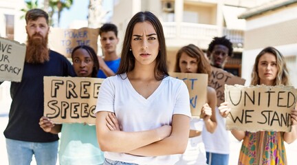 Wall Mural - Young activist woman with arms crossed gesture standing with a group of protesters holding banner protesting at the city.