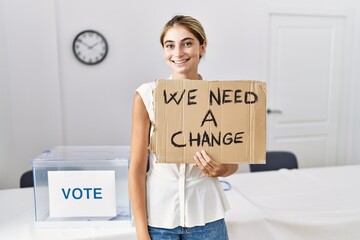 Poster - Young blonde woman at political election holding we need a change banner looking positive and happy standing and smiling with a confident smile showing teeth