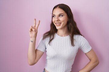 Sticker - Young hispanic girl standing over pink background smiling looking to the camera showing fingers doing victory sign. number two.