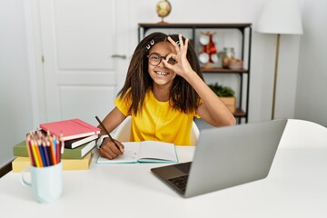 Sticker - Young african american girl doing homework at home doing ok gesture with hand smiling, eye looking through fingers with happy face.