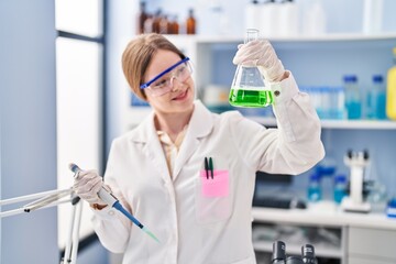 Sticker - Young blonde woman wearing scientist uniform measuring liquid on test tube at laboratory