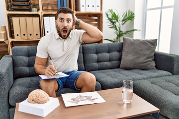 Canvas Print - Handsome hispanic man working with rorschach test at psychology clinic crazy and scared with hands on head, afraid and surprised of shock with open mouth