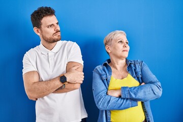 Poster - Young brazilian mother and son standing over blue background looking to the side with arms crossed convinced and confident