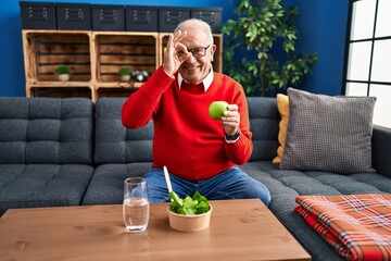 Canvas Print - Senior man with grey hair eating salad and green apple smiling happy doing ok sign with hand on eye looking through fingers