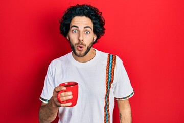 Poster - Handsome hispanic man drinking a cup coffee scared and amazed with open mouth for surprise, disbelief face