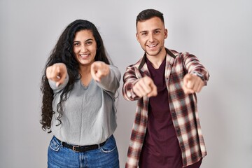 Sticker - Young hispanic couple standing over white background pointing to you and the camera with fingers, smiling positive and cheerful